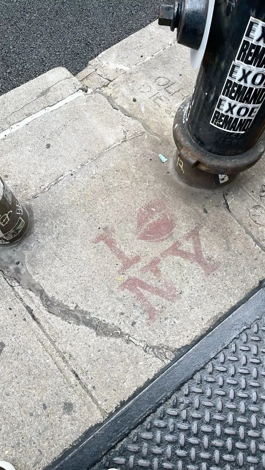 A red I love NY stencil painted on a concrete sidewalk next to a fire hydrant covered in stickers.
